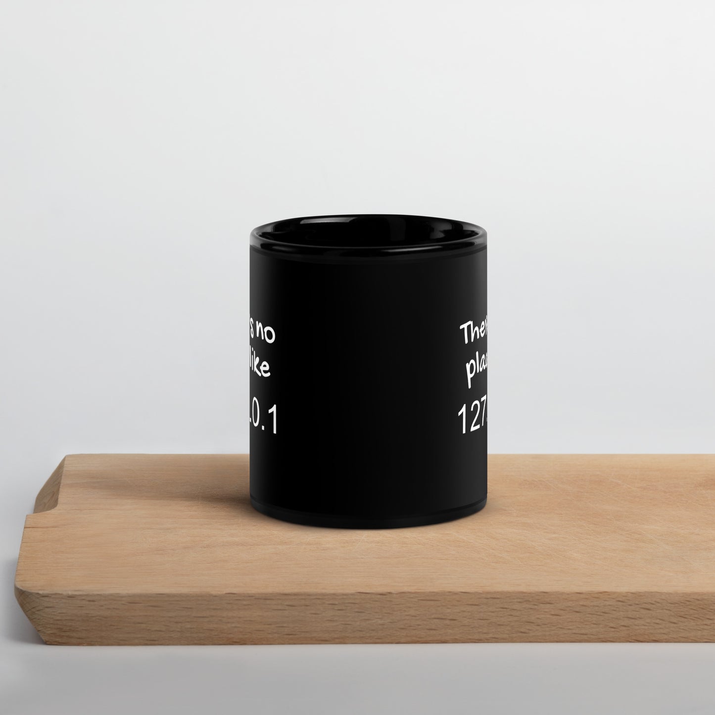 Black 11oz tech humor coffee mug with the slogan ‘There's no place like 127.0.0.1’ on cutting board.