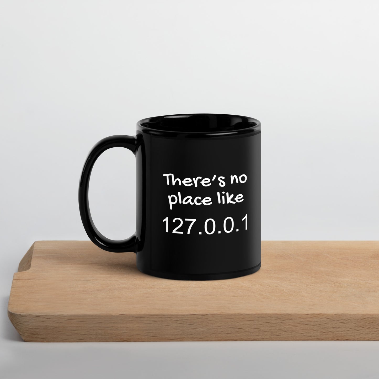 Black 11oz tech humor coffee mug with the slogan ‘There's no place like 127.0.0.1’ with handle on left on cutting board.
