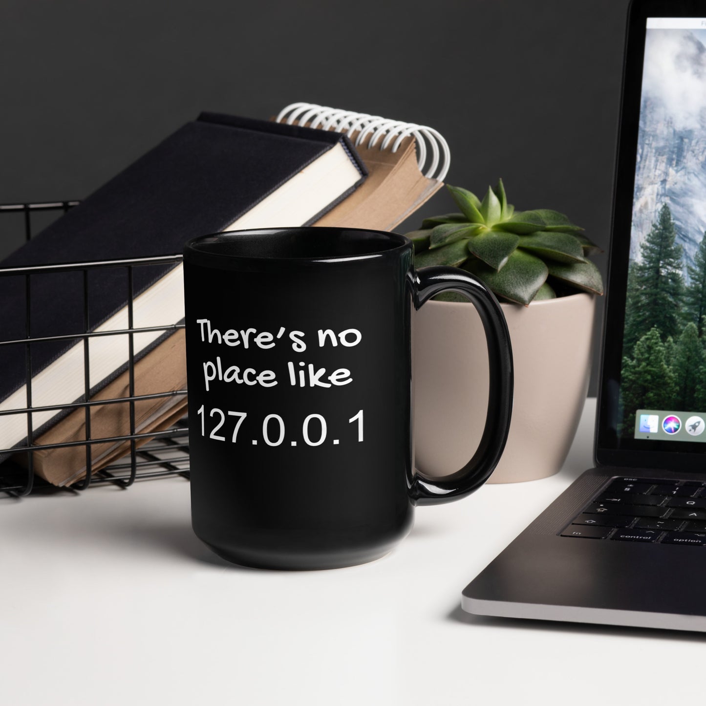 Black 15oz tech humor coffee mug with the slogan ‘There's no place like 127.0.0.1’ with handle on right on desk.