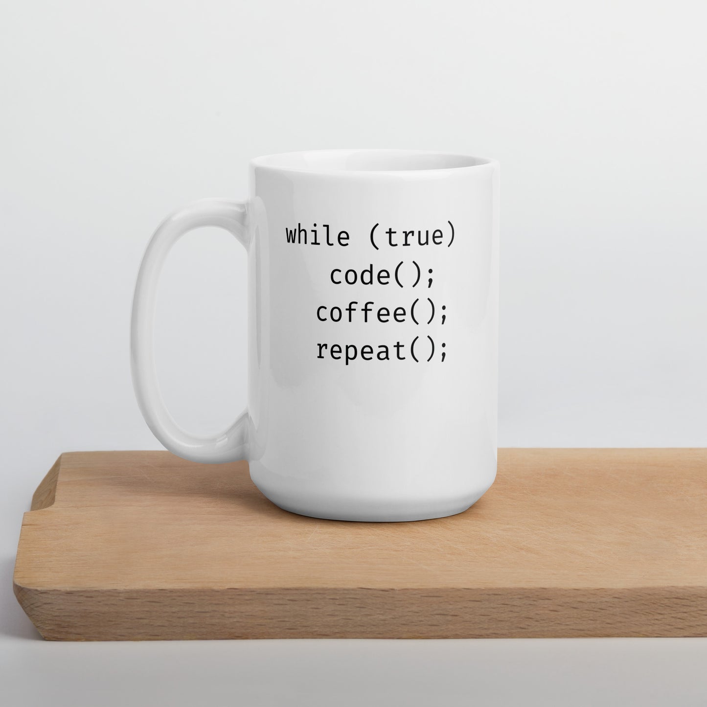 White 15oz tech humor coffee mug featuring slogan “Code. Coffee. Repeat.” in code with handle on the left on cutting board.
