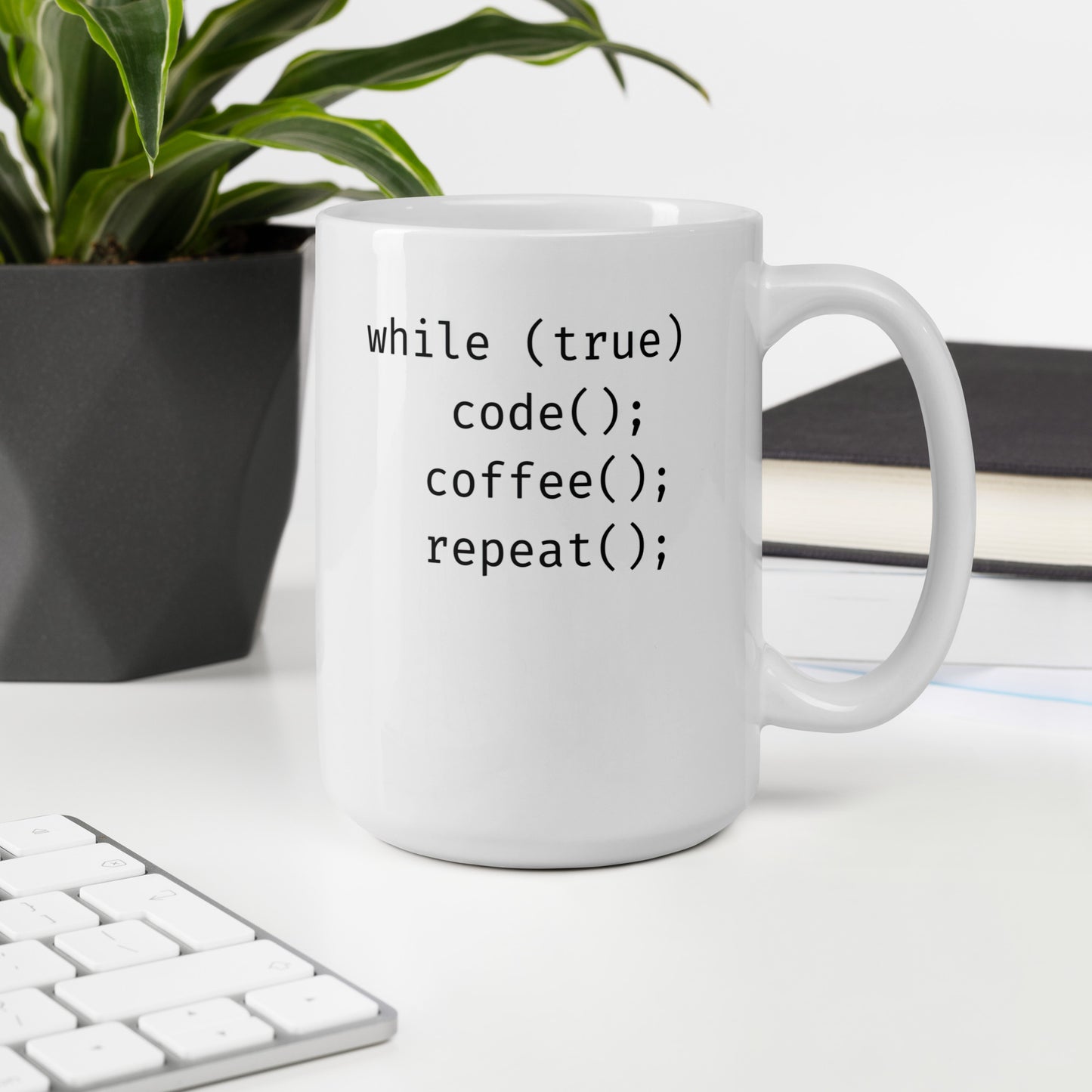 White 15oz tech humor coffee mug featuring slogan “Code. Coffee. Repeat.” in code with handle on the right on desk.