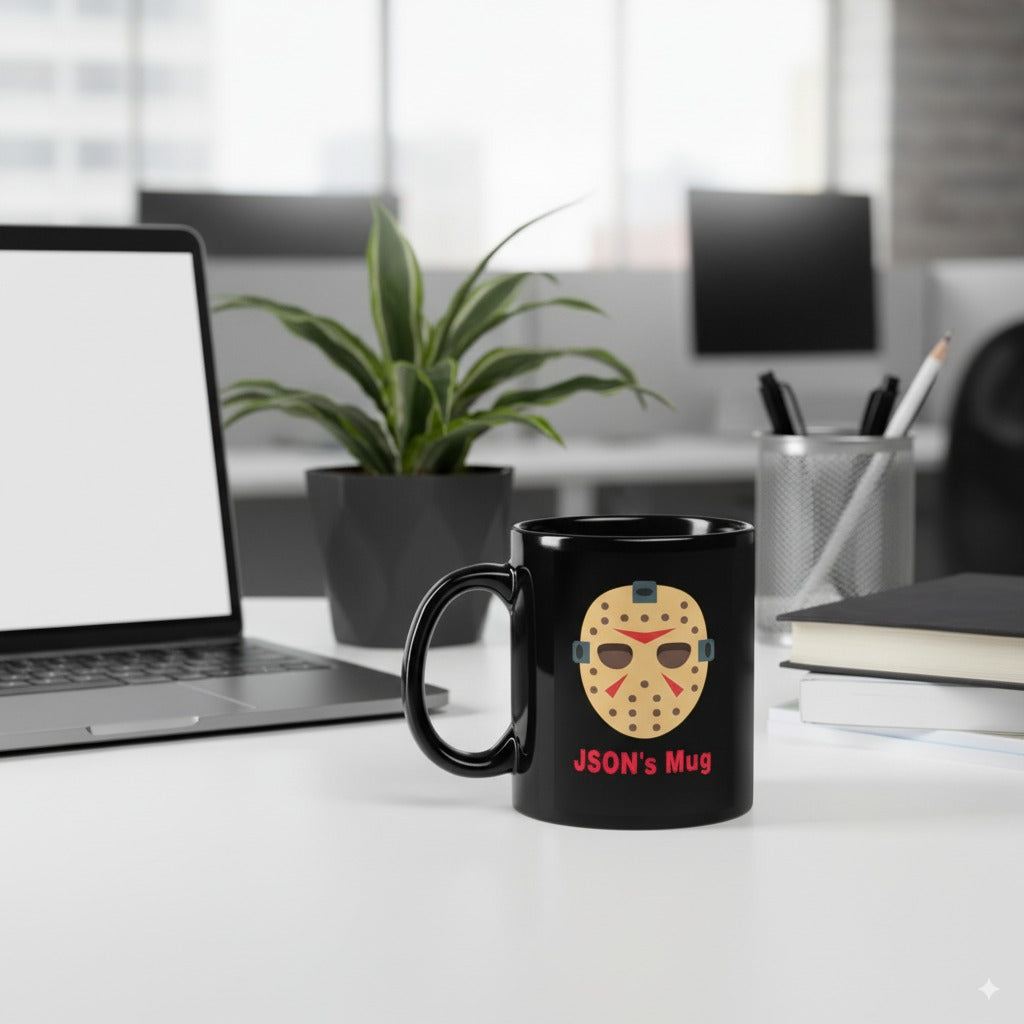 Black mug with a Jason Voorhees design on a desk with a laptop and office items.