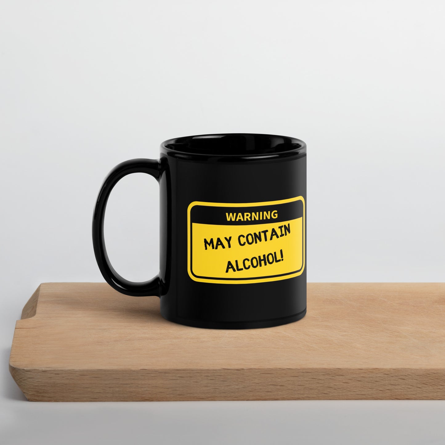 Black 11oz tech humor coffee mug with name label that says, ‘Warning: May Contain Alcohol!’ with handle on left on cutting board.