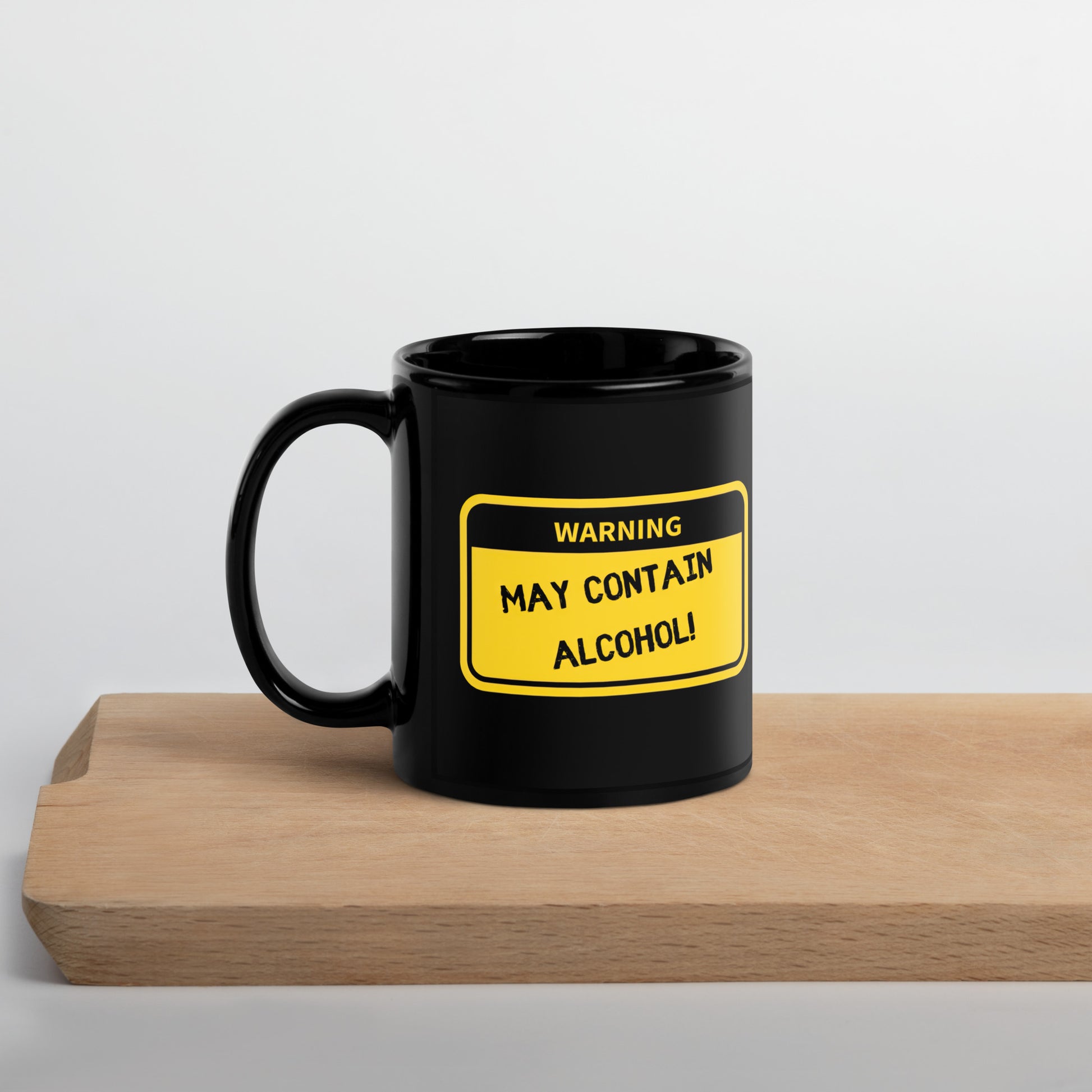 Black 11oz tech humor coffee mug with name label that says, ‘Warning: May Contain Alcohol!’ with handle on left on cutting board.