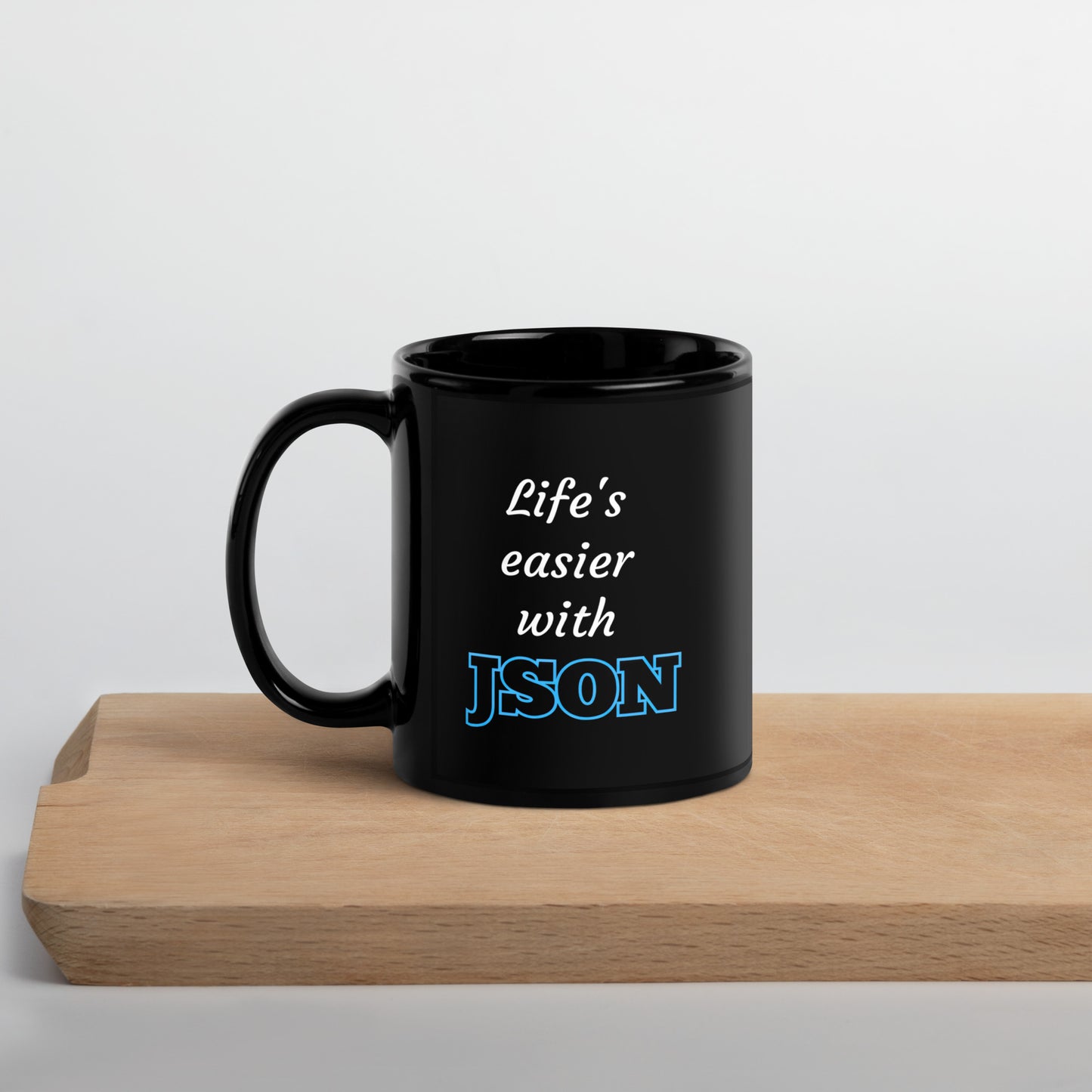 Black 11oz tech humor coffee mug with design that reads ‘Life's easier with JSON’ with handle on the left on cutting board.