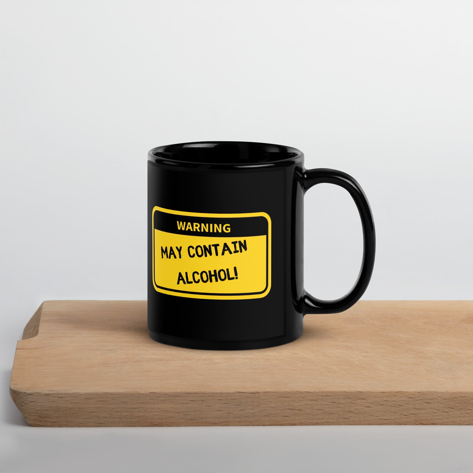 Black 11oz tech humor coffee mug with name label that says, ‘Warning: May Contain Alcohol!’ with handle on right on cutting board.