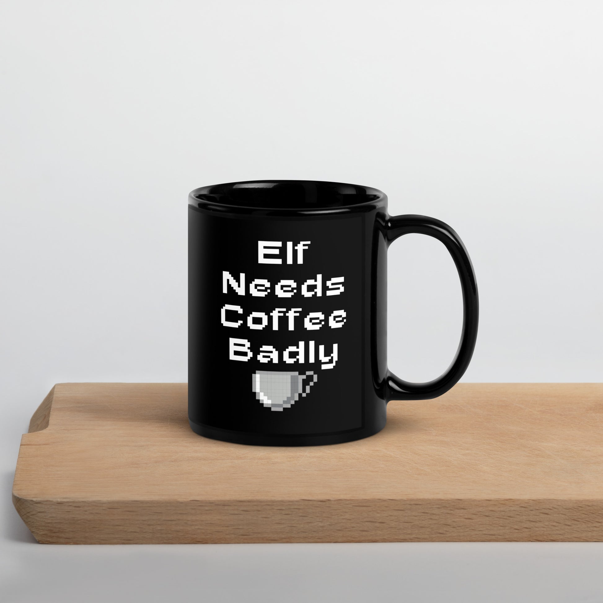 Black 11oz retro coffee mug featuring an ‘Elf Needs Coffee Badly’ video game design with handle on the right on cutting board.