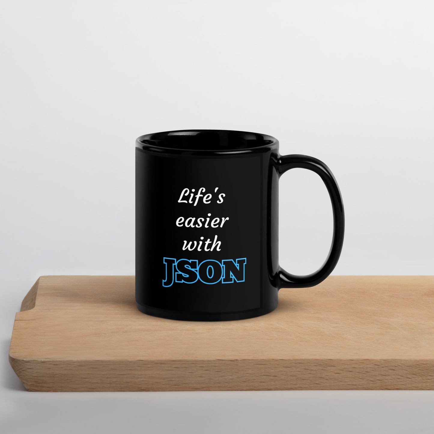 Black 11oz tech humor coffee mug with design that reads ‘Life's easier with JSON’ with handle on the right on cutting board.