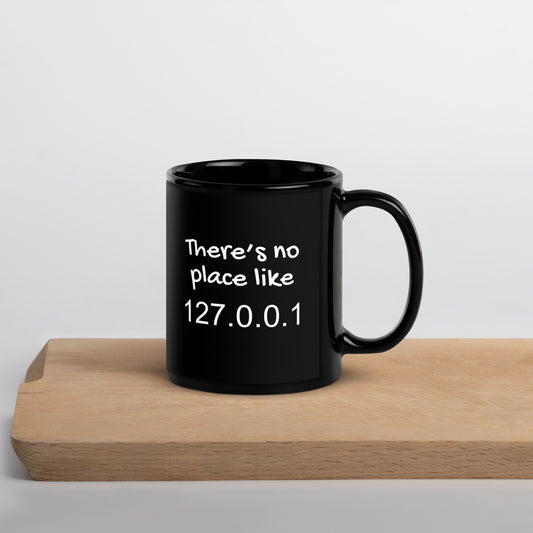 Black 11oz tech humor coffee mug with the slogan ‘There's no place like 127.0.0.1’ with handle on right on cutting board.