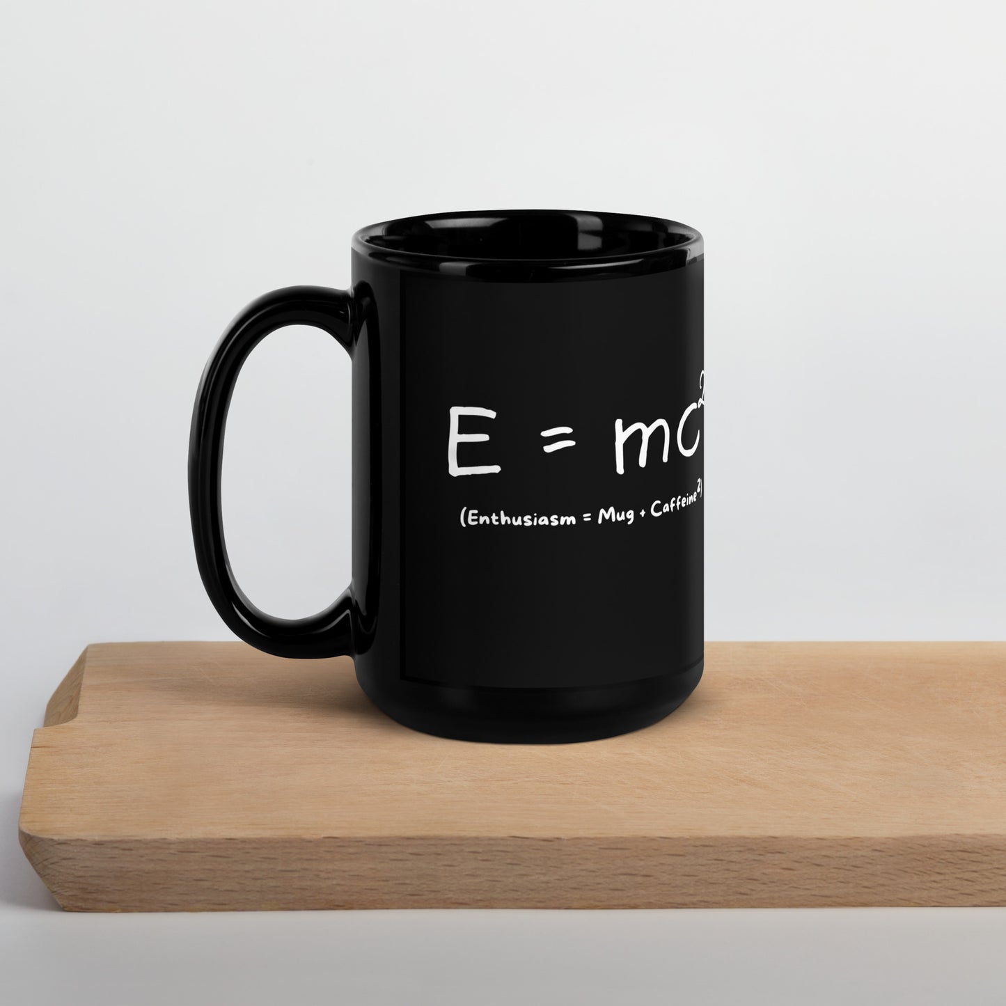 Black 15oz tech humor coffee mug featuring an ‘E=mc2’ design with handle on the left on cutting board.