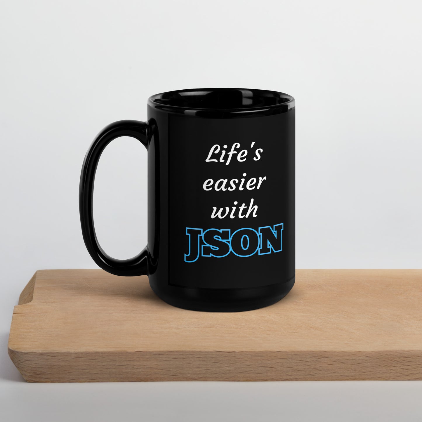 Black 15oz tech humor coffee mug with design that reads ‘Life's easier with JSON’ with handle on the left on cutting board.