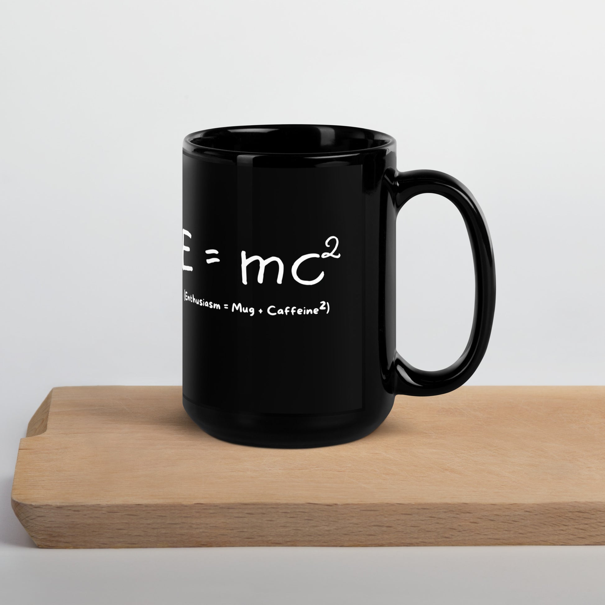 Black 15oz tech humor coffee mug featuring an ‘E=mc2’ design with handle on the right on cutting board.