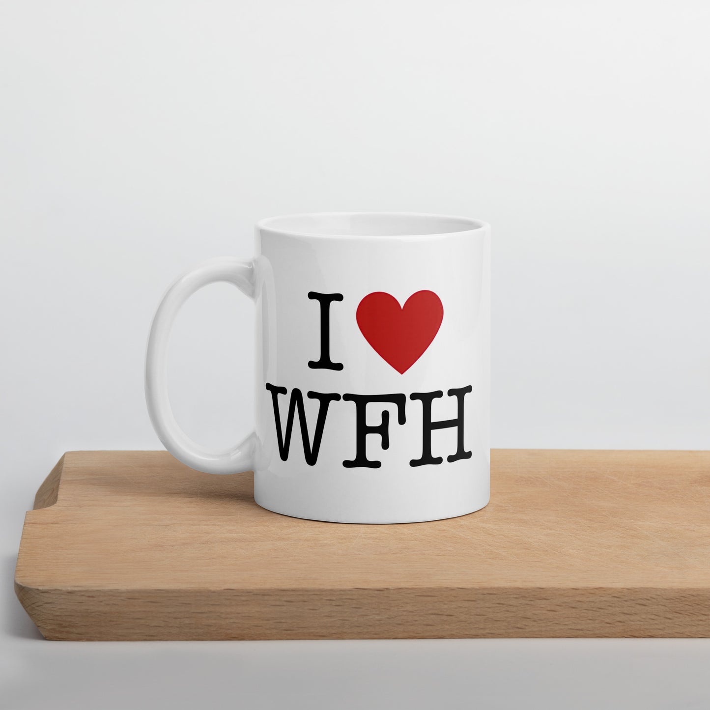 White 11oz tech humor coffee mug with an I Love NY style design that reads ‘I Love WFH’ with handle on left on cutting board.