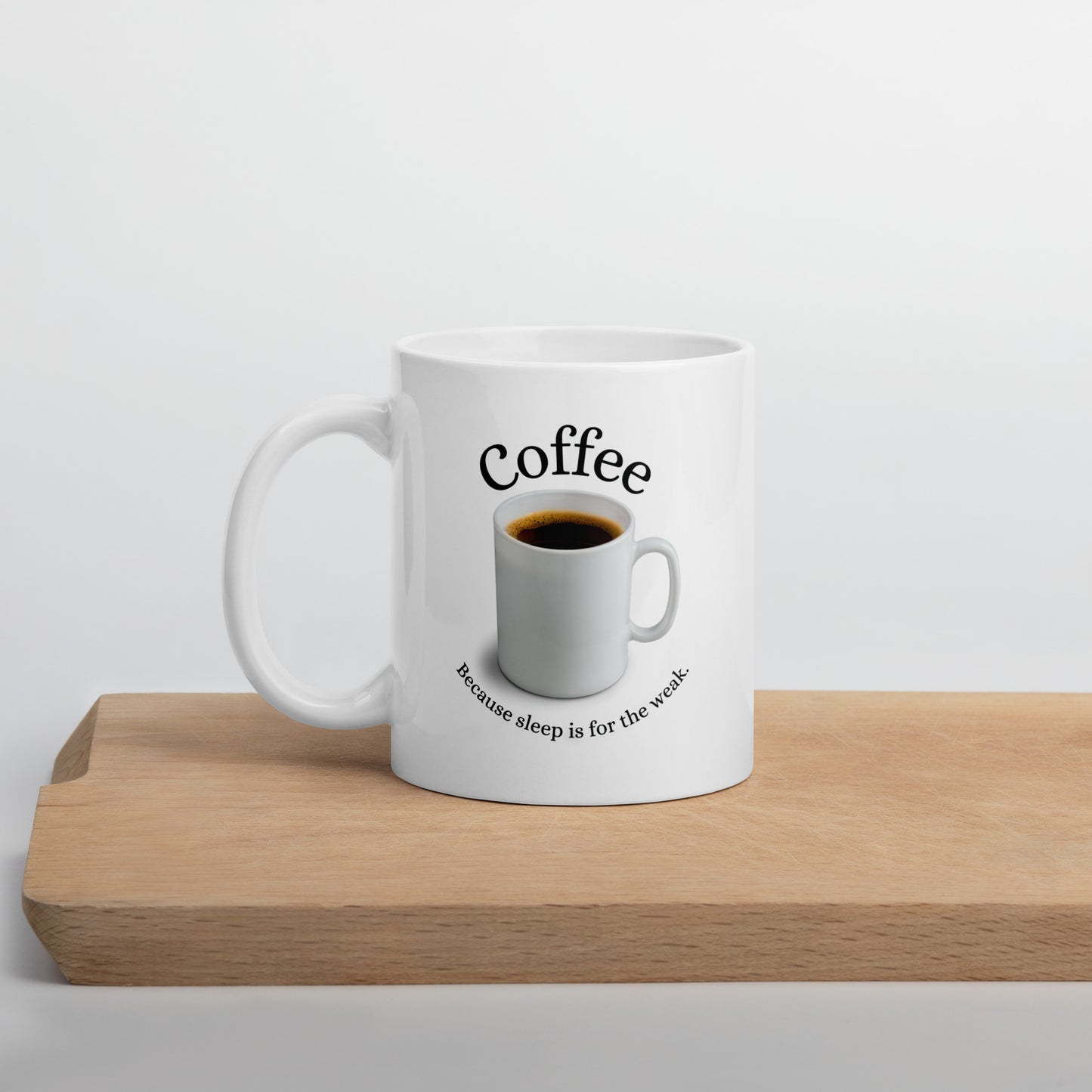 White 11oz tech humor coffee mug featuring slogan “Coffee: Because Sleep is for the Weak” with handle on the left on cutting board.