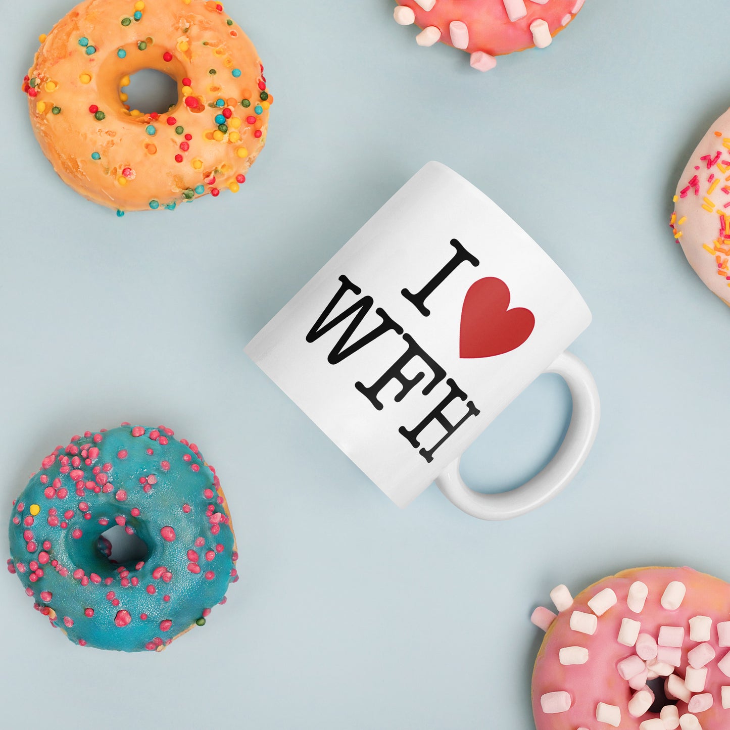 White 11oz tech humor coffee mug with an I Love NY style design that reads ‘I Love WFH’ with handle on right amongst donuts.