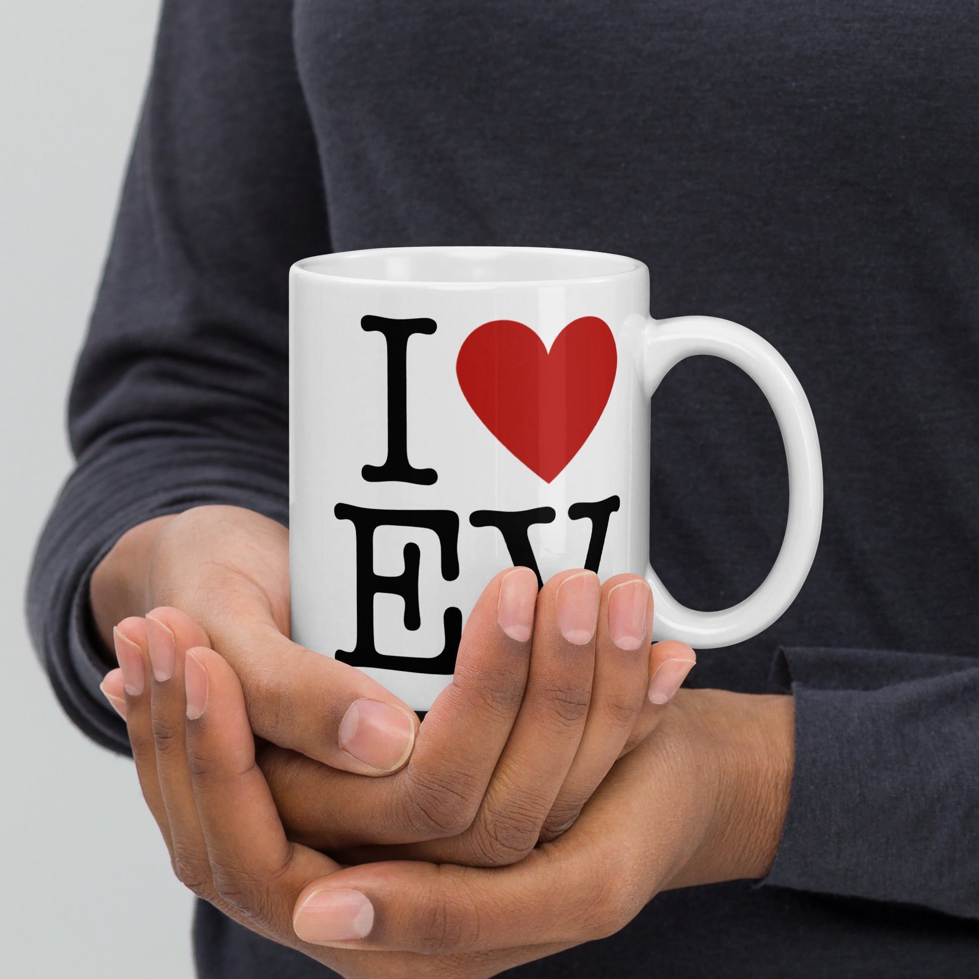 White 11oz EV themed coffee mug with an I Love NY type slogan ‘I Love EV’ with handle on right held by man.