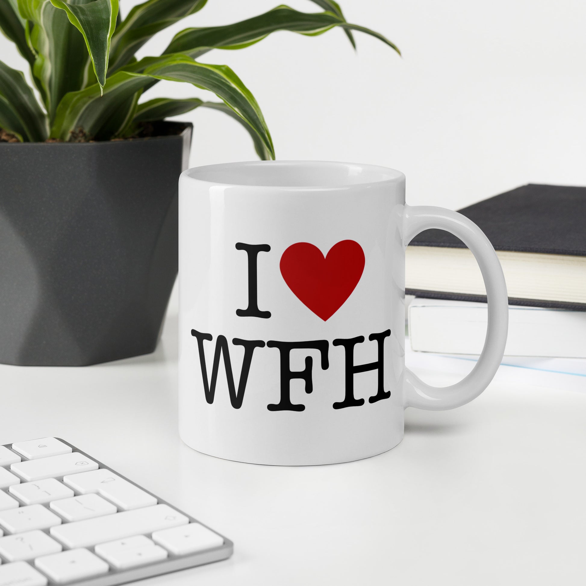 White 11oz tech humor coffee mug with an I Love NY style design that reads ‘I Love WFH’ with handle on right on desk.