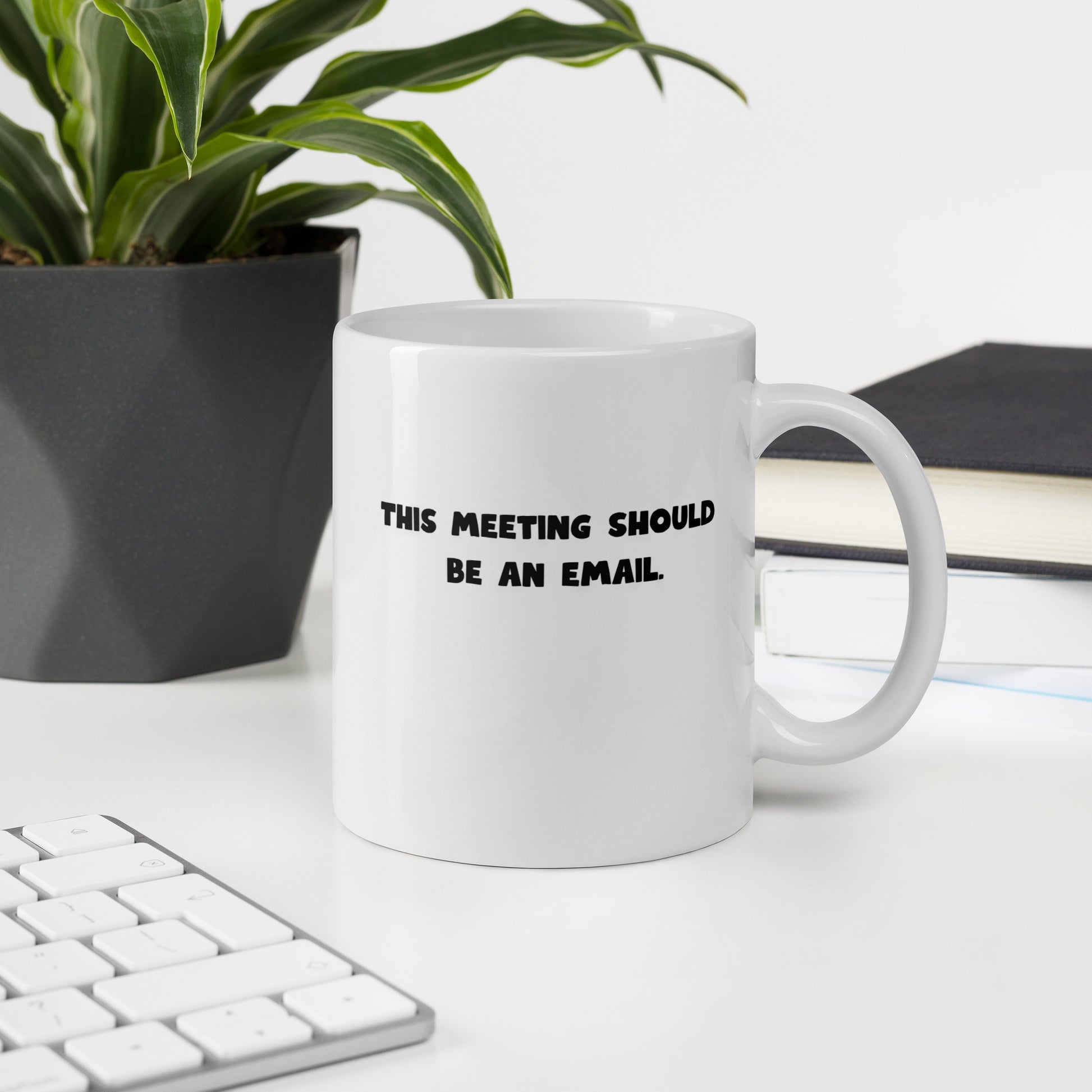 White 11oz tech humor coffee mug with the slogan ‘This Meeting Should Be An Email’ with handle on right on office desk.