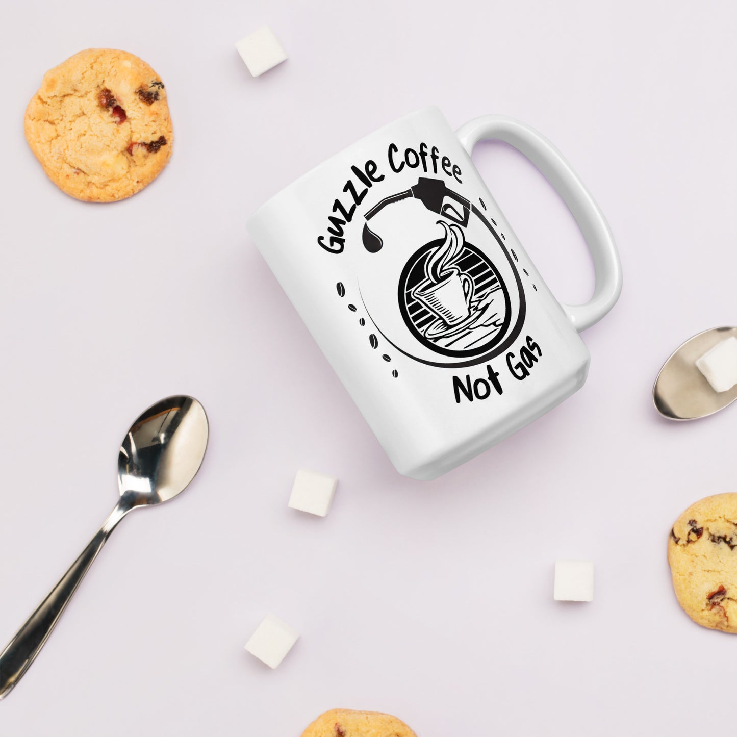 White 15oz EV themed coffee mug with a gas pump over a coffee cup and slogan ‘Guzzle Coffee, Not Gas’ among biscuits and spoons.