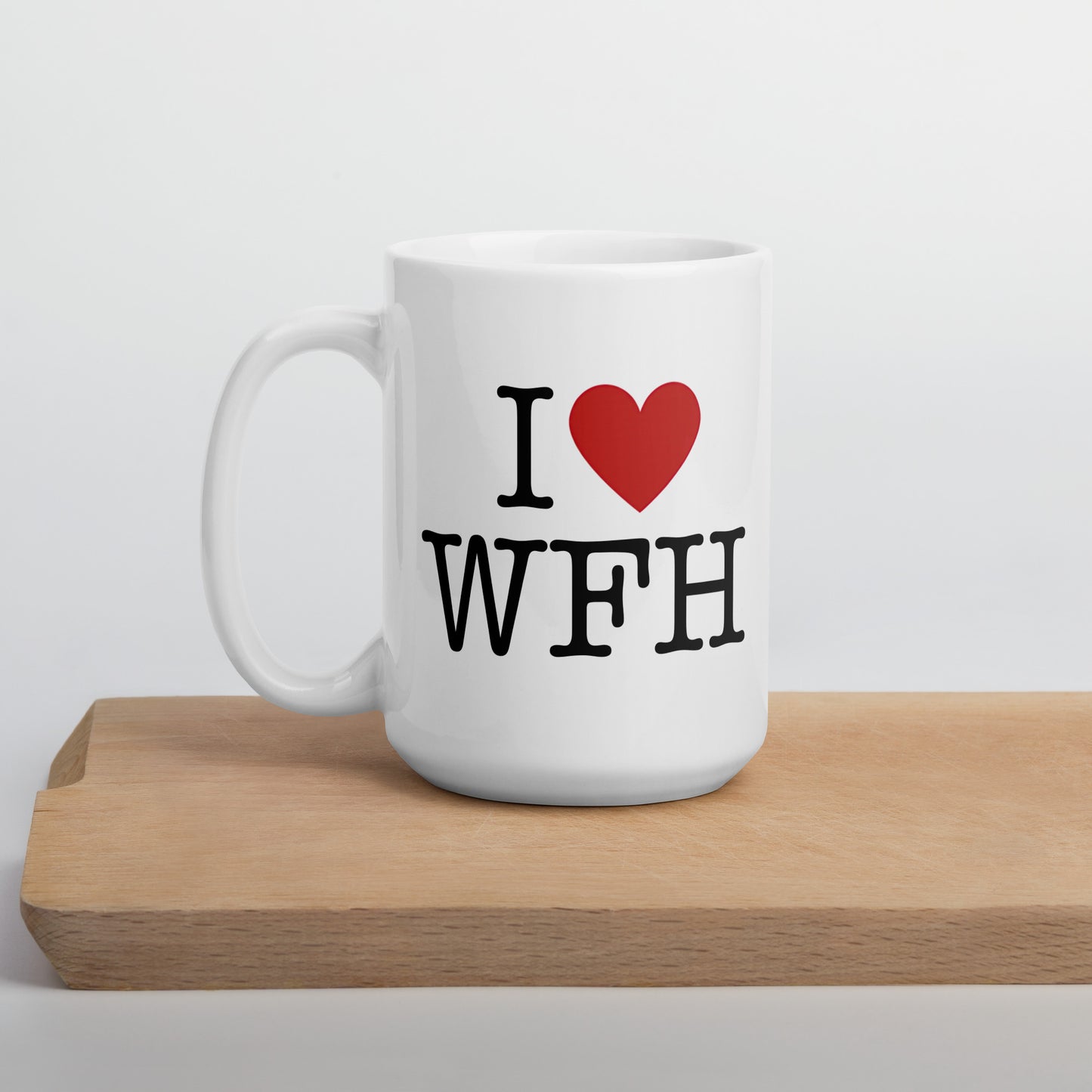 White 15oz tech humor coffee mug with an I Love NY style design that reads ‘I Love WFH’ with handle on left on cutting board.