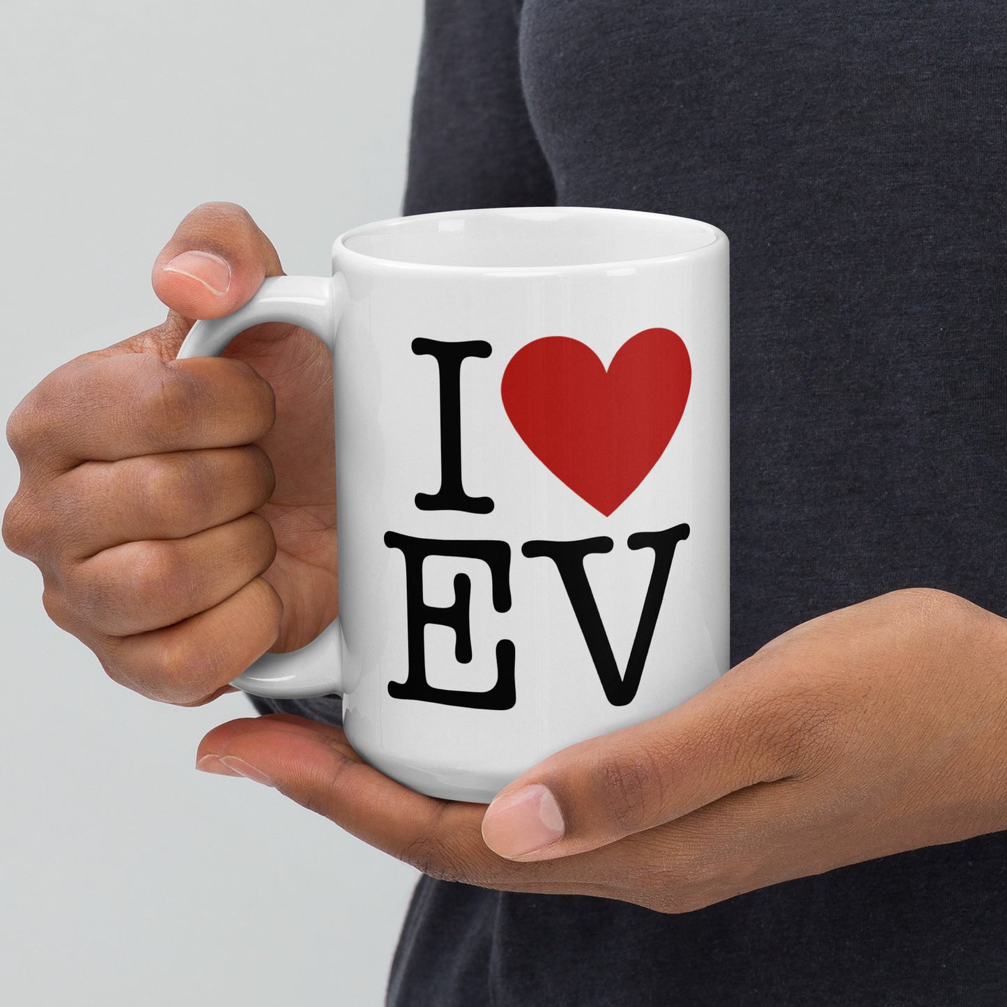 White 15oz EV themed coffee mug with an I Love NY type slogan ‘I Love EV’ with handle on left held by a man.