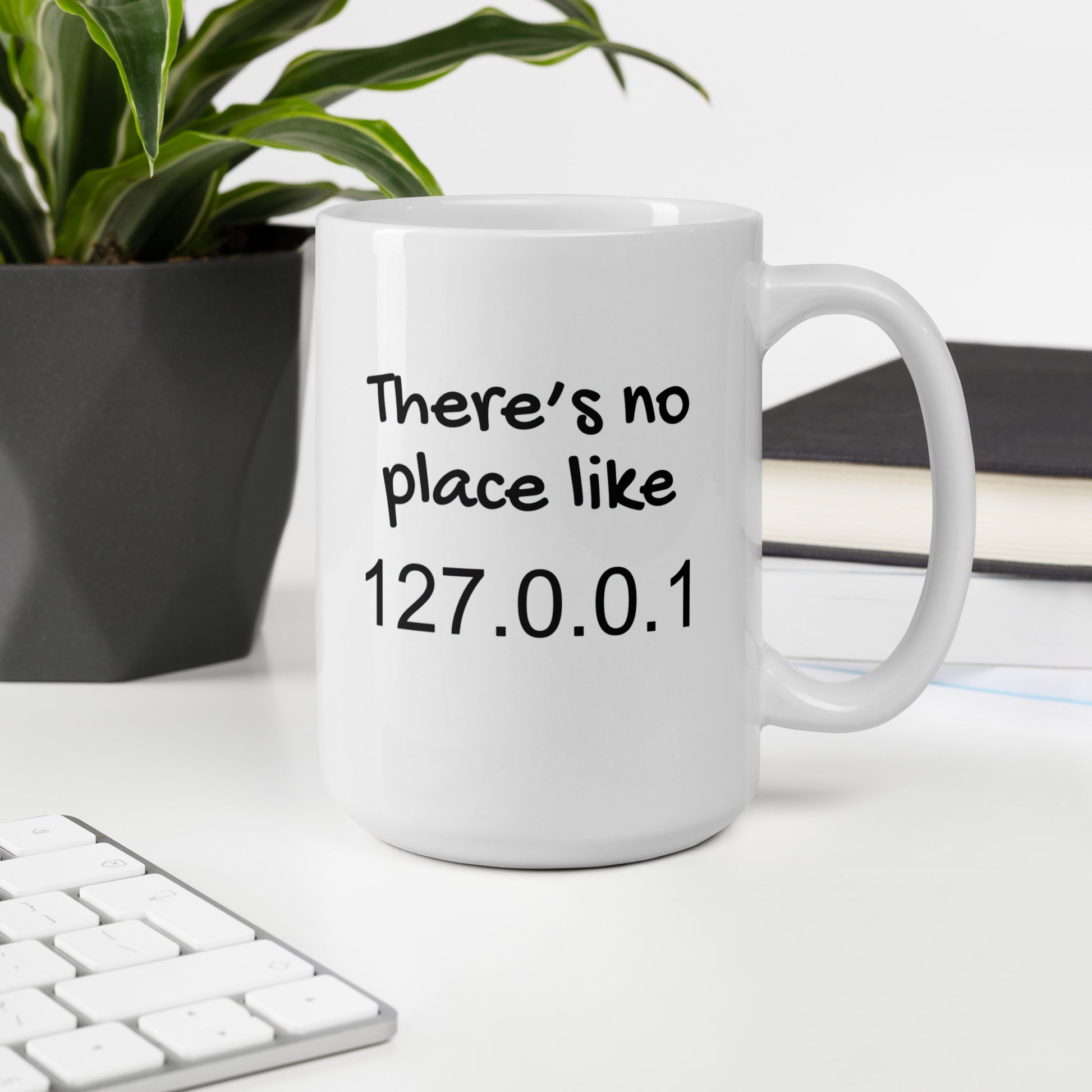 White 15oz tech humor coffee mug with the slogan ‘There's no place like 127.0.0.1’ with handle on right on desk.